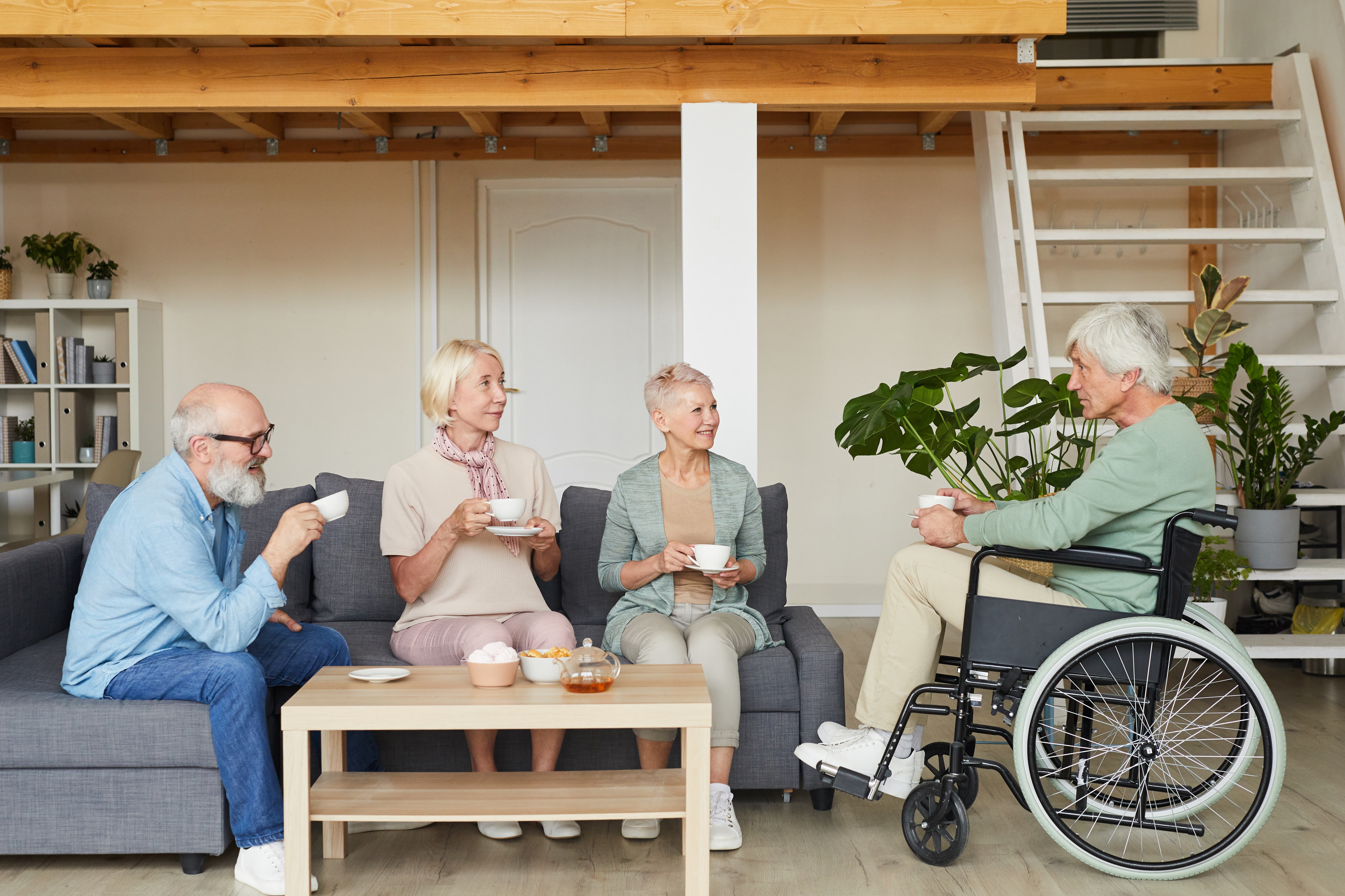 group senior friends talking disabled man drinking tea together living room  1 